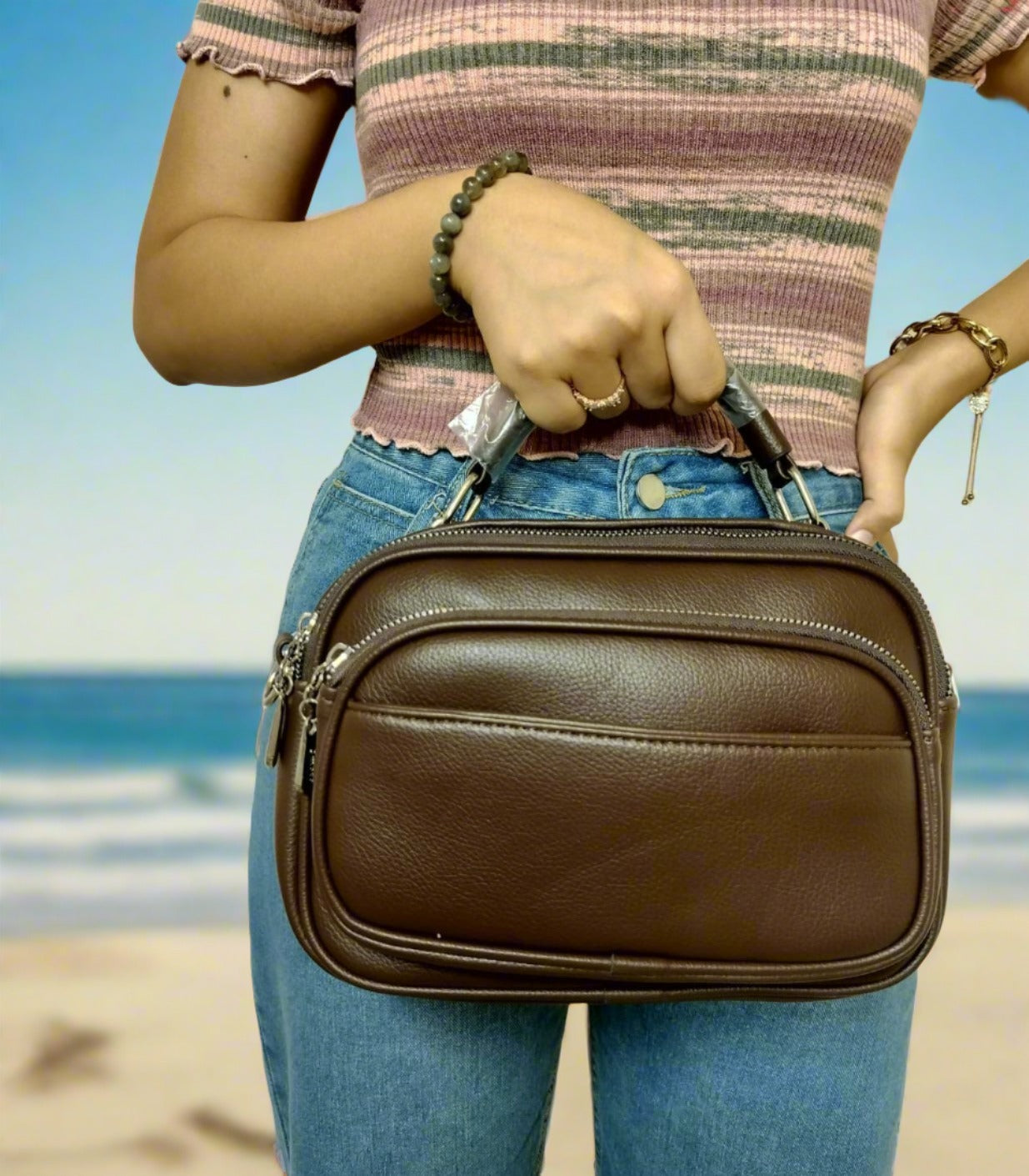 Brown leather bag with double zipper pockets held by person wearing pink striped top and jeans