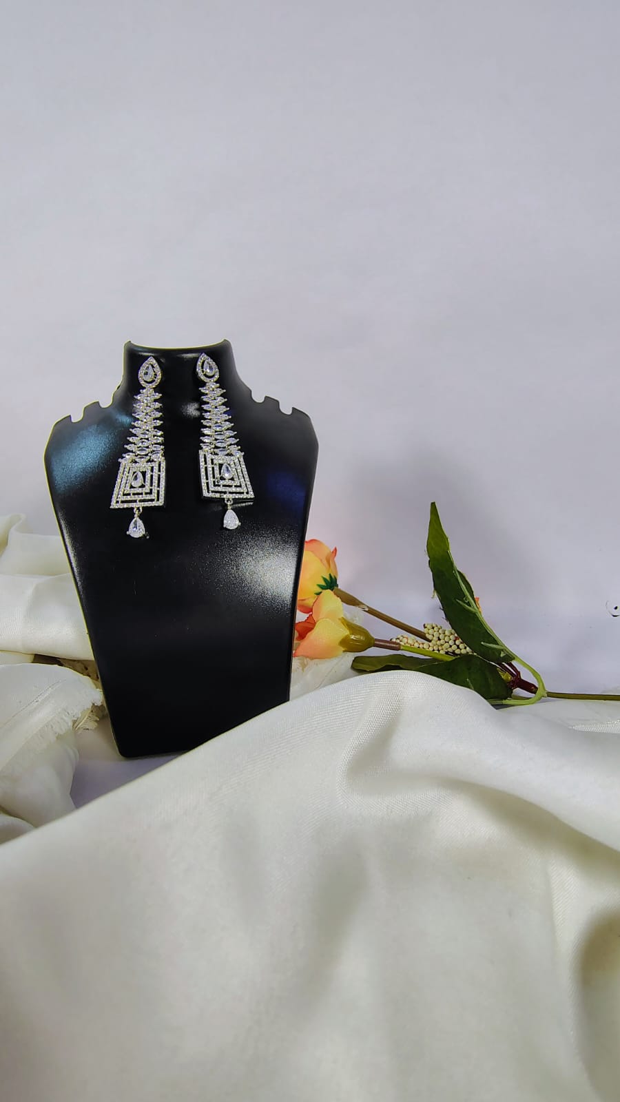 Designer American diamond dangle earrings displayed on a black stand with floral background