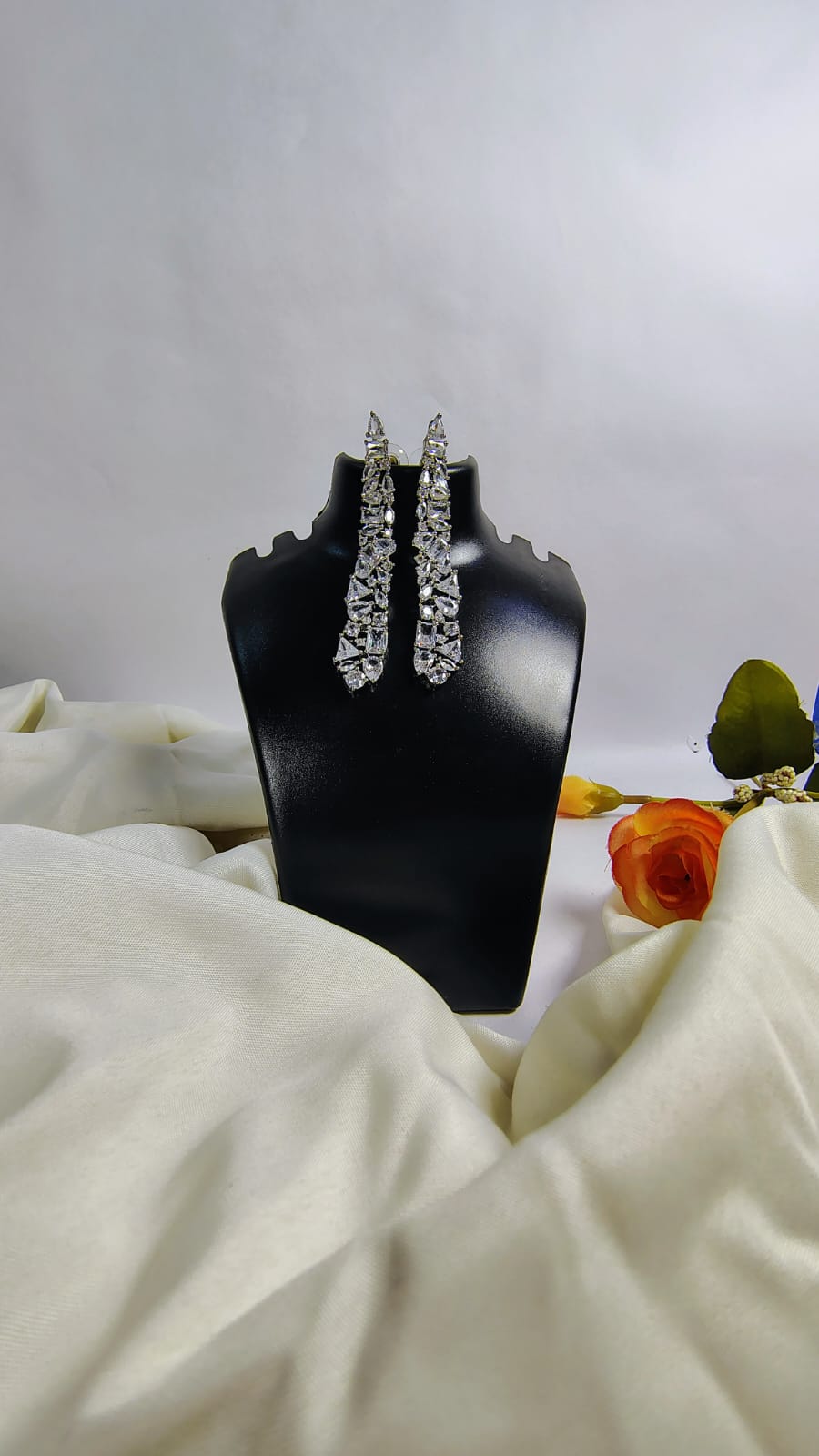 Wincham Fashion House designer American diamond dangle earrings displayed on black stand with floral decor
