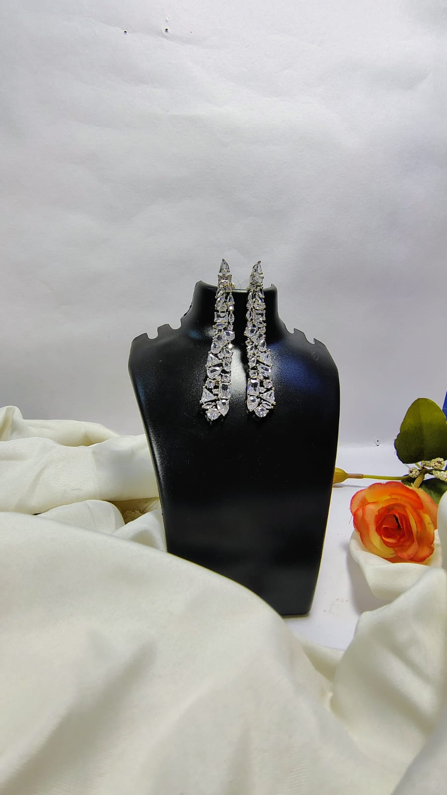 Designer American diamond dangle earrings displayed on black stand with white cloth and orange flower
