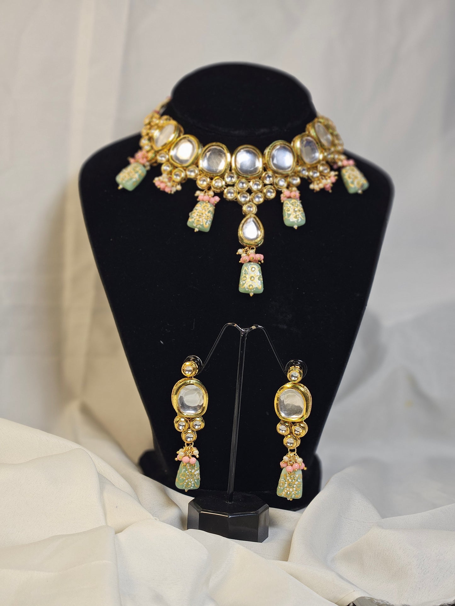 Pink and green Indian jewelry set with necklace and matching earrings displayed on black stand