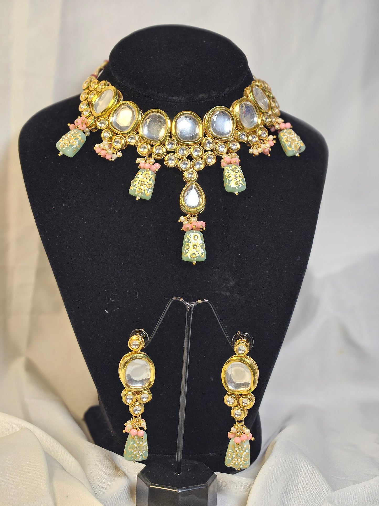 Pink and green Indian jewelry set with gold accents displayed on black stand by Wincham Fashion House