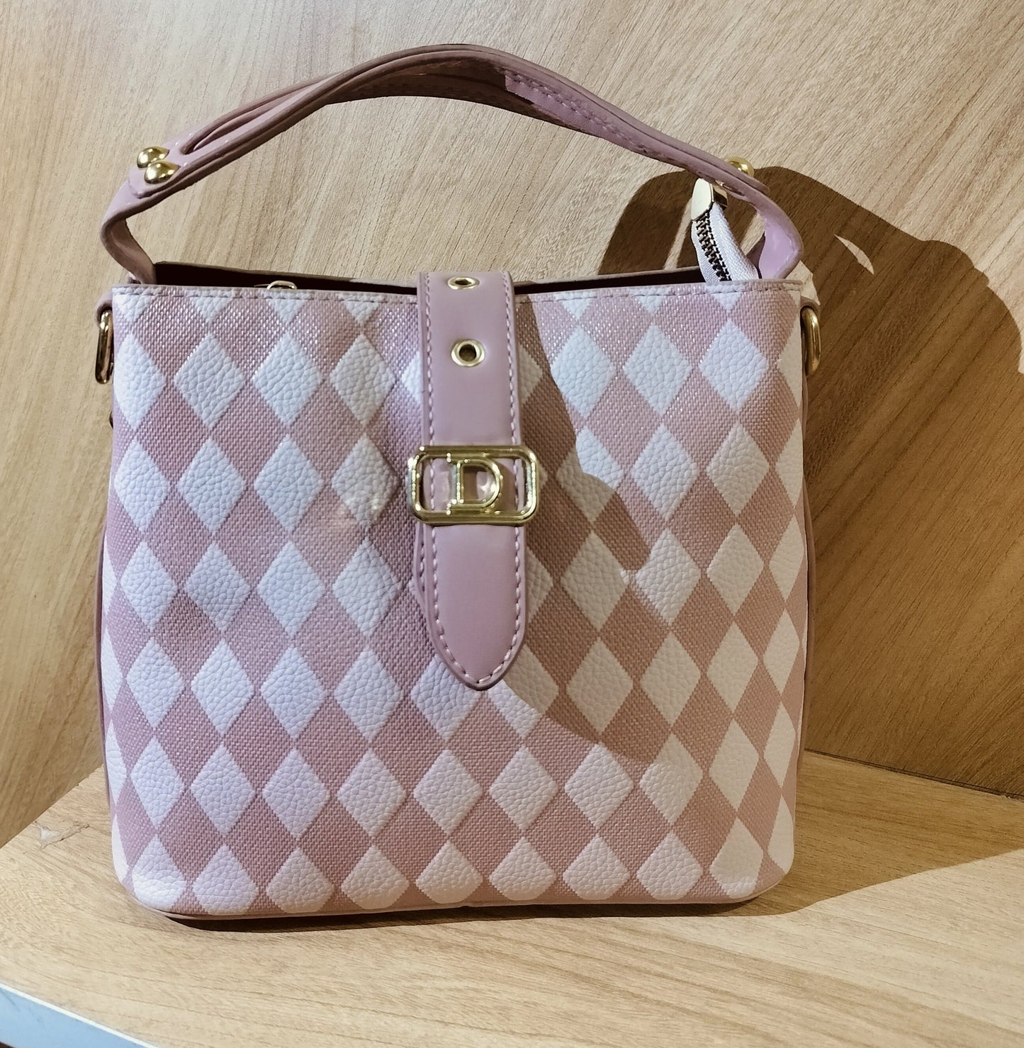 Pink leather purse for women with diamond pattern and gold buckle on wooden surface