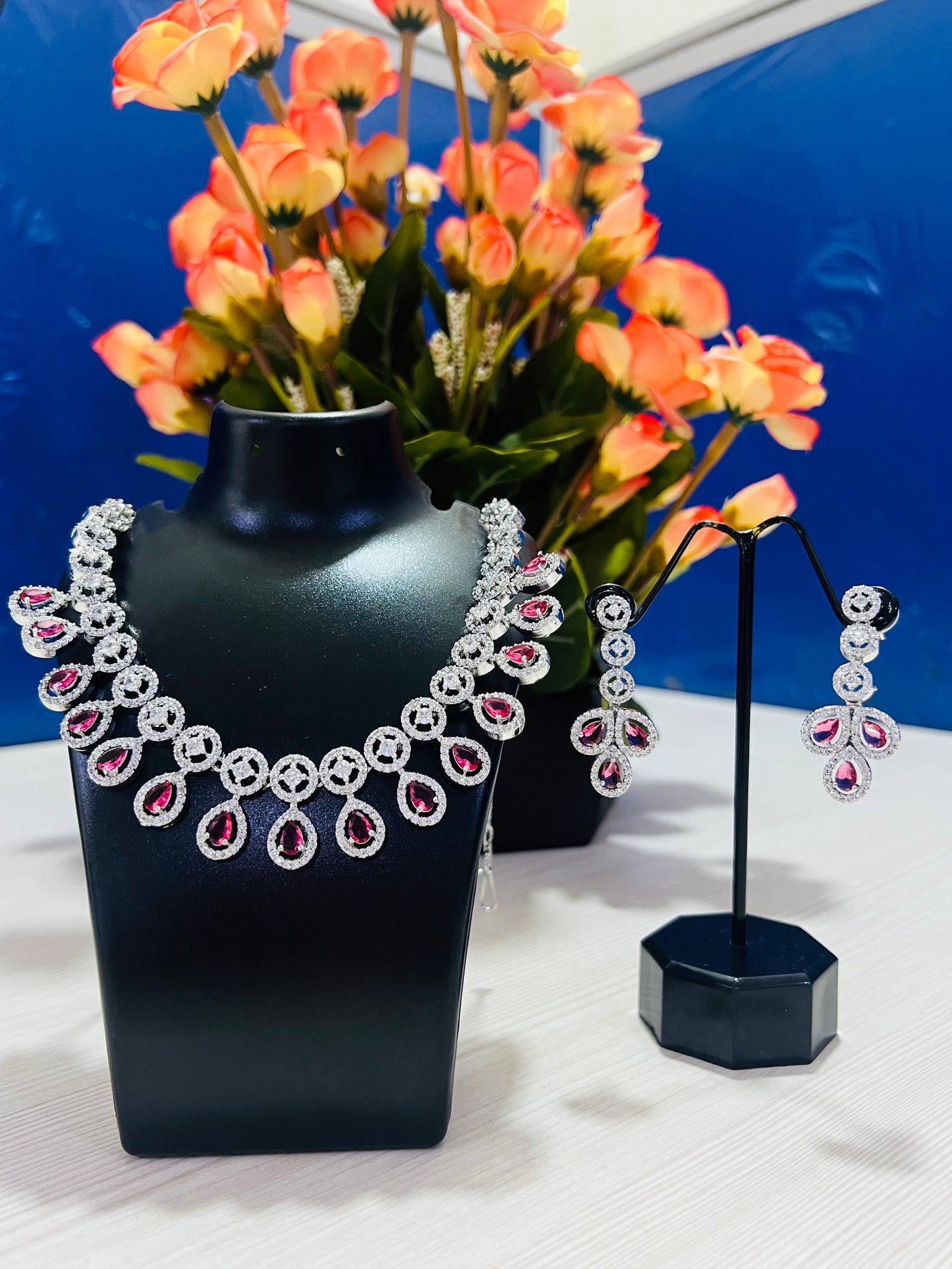 Ruby leaf crystal necklace set displayed on black stand with matching earrings and floral background