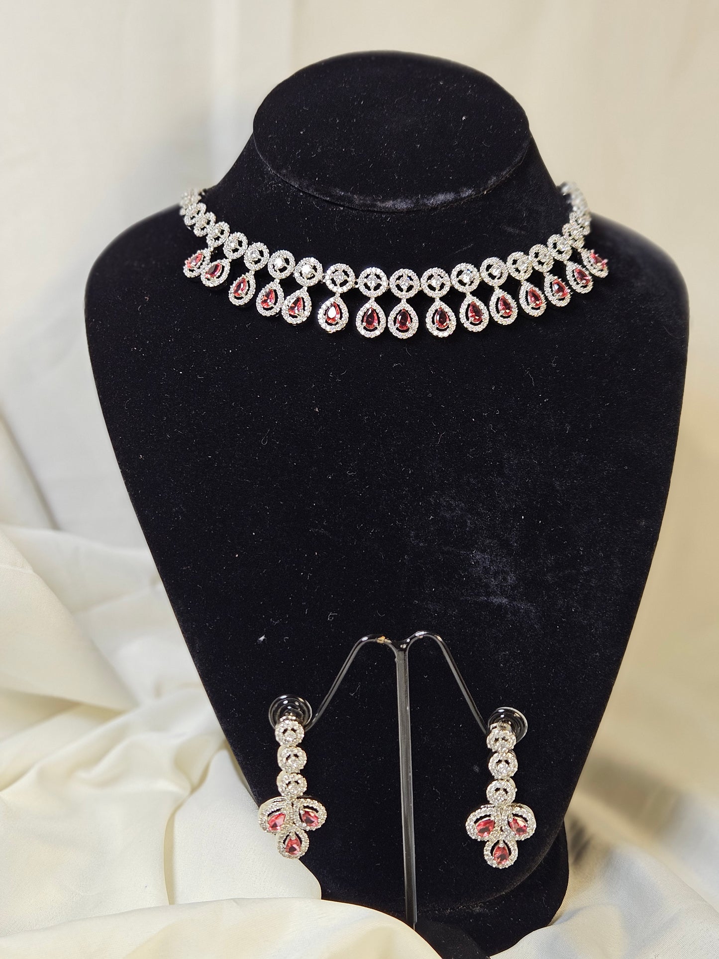 Elegant ruby leaf crystal necklace set with matching earrings displayed on black stand