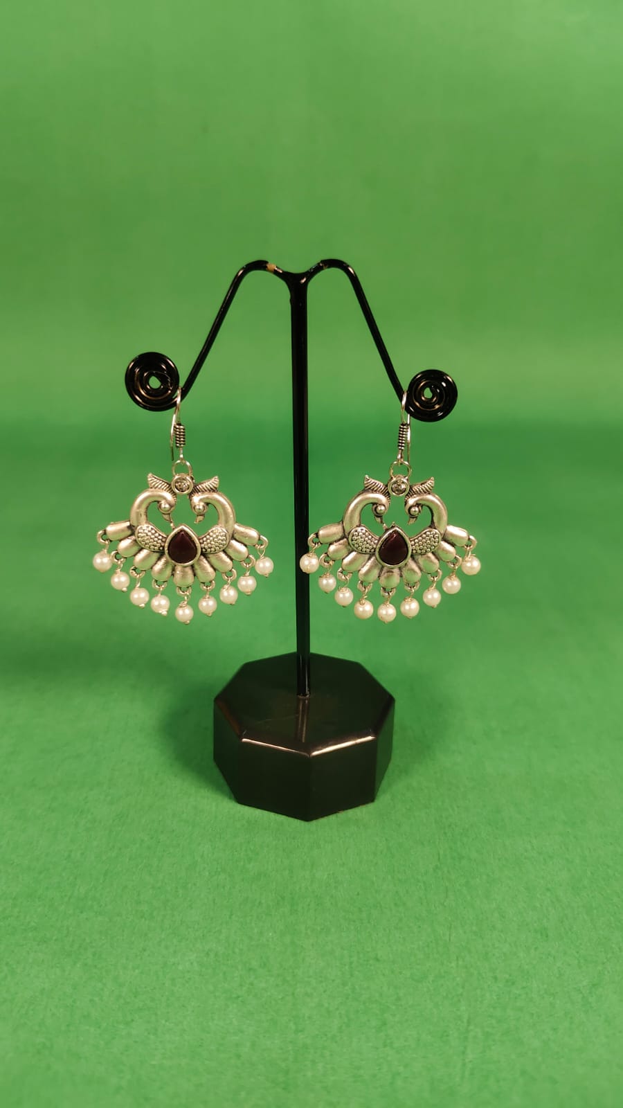 Silver alloy Green hanging earrings with intricate design and pearl accents displayed on black stand