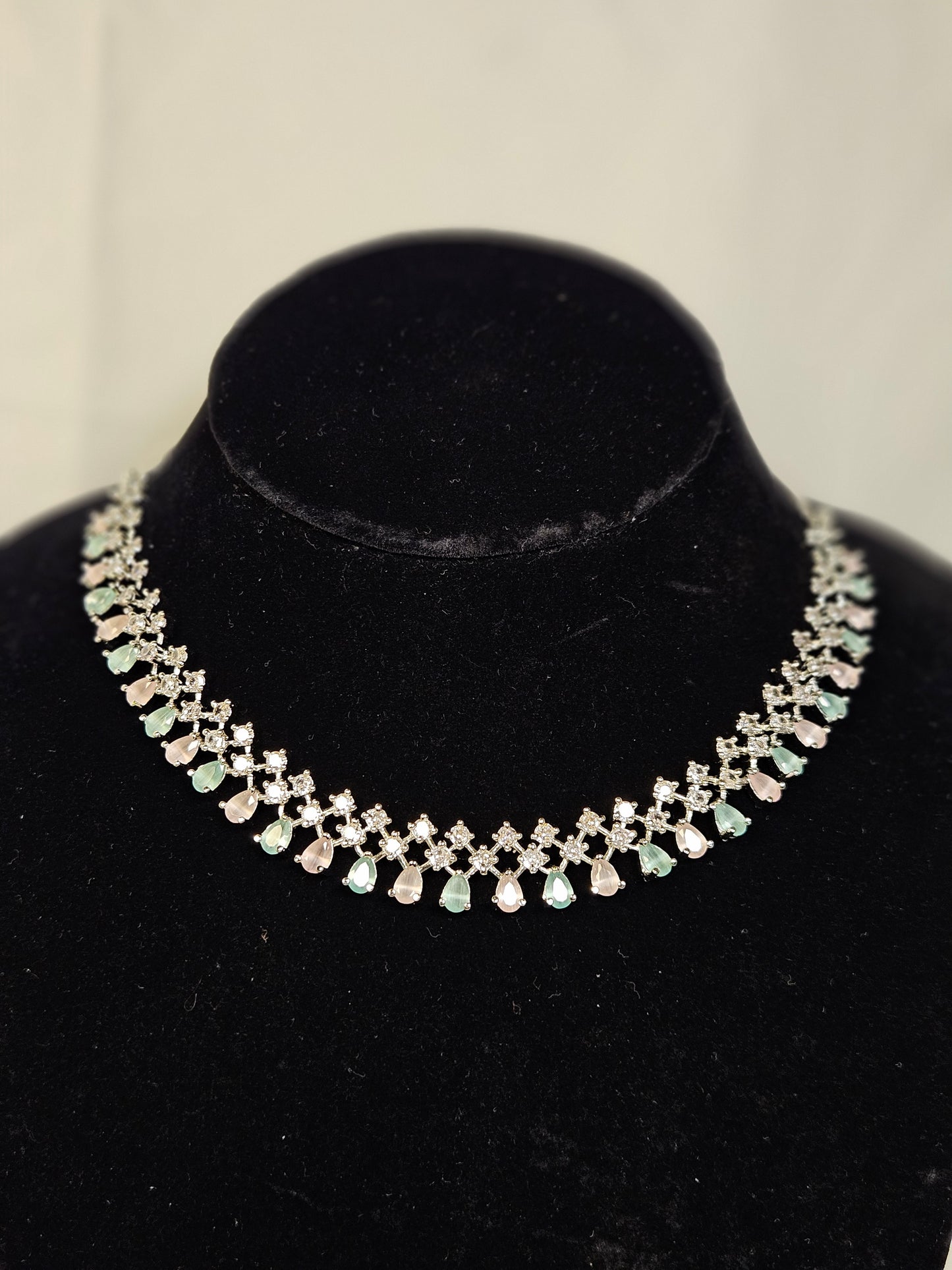Elegant American diamond necklace set with alternating clear and green stones displayed on black velvet stand