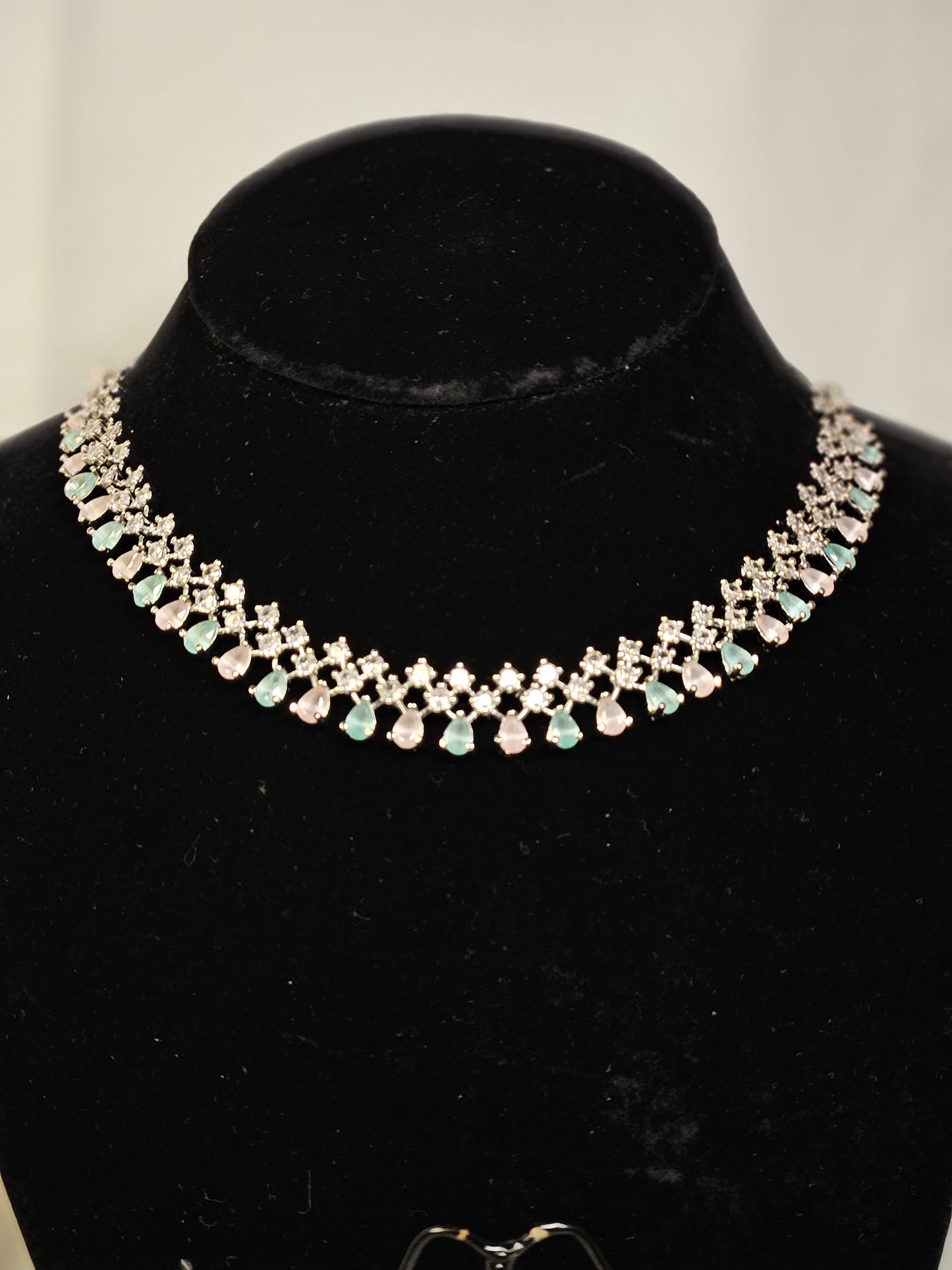 Wincham Fashion House American diamond necklace set with clear and green stones on black display