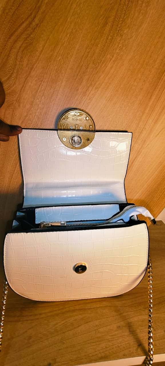 Open white party sling purse with chain strap and black interior lining on wooden surface