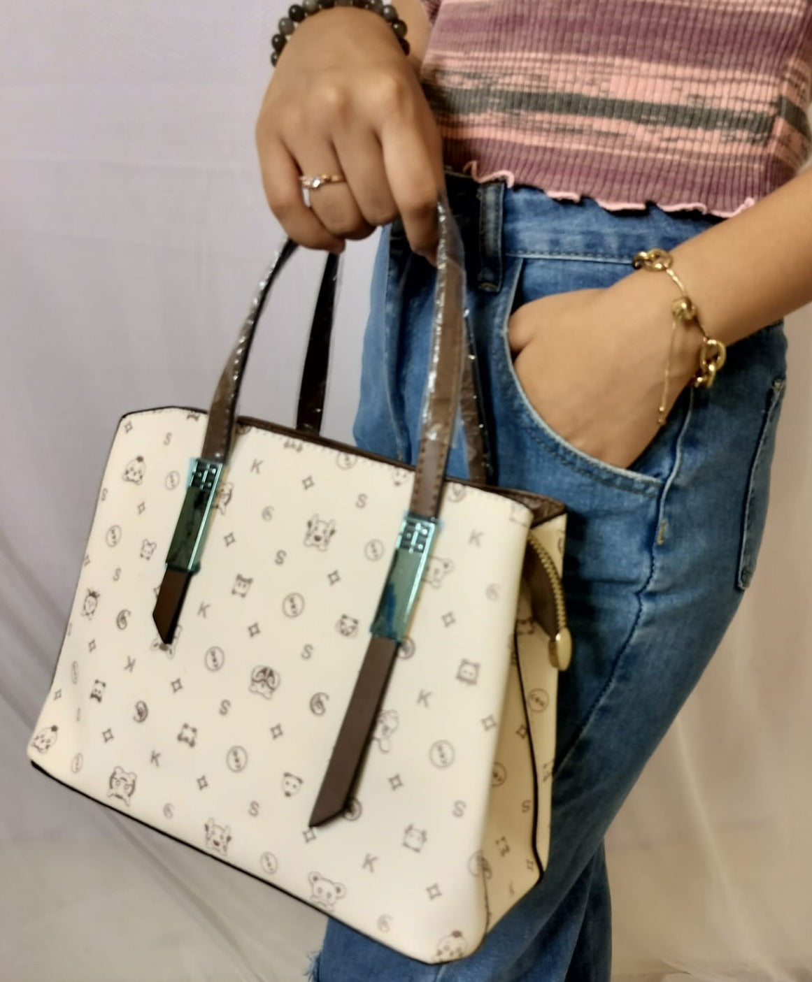 White patterned handbag with brown handles held by a woman in jeans and a pink top