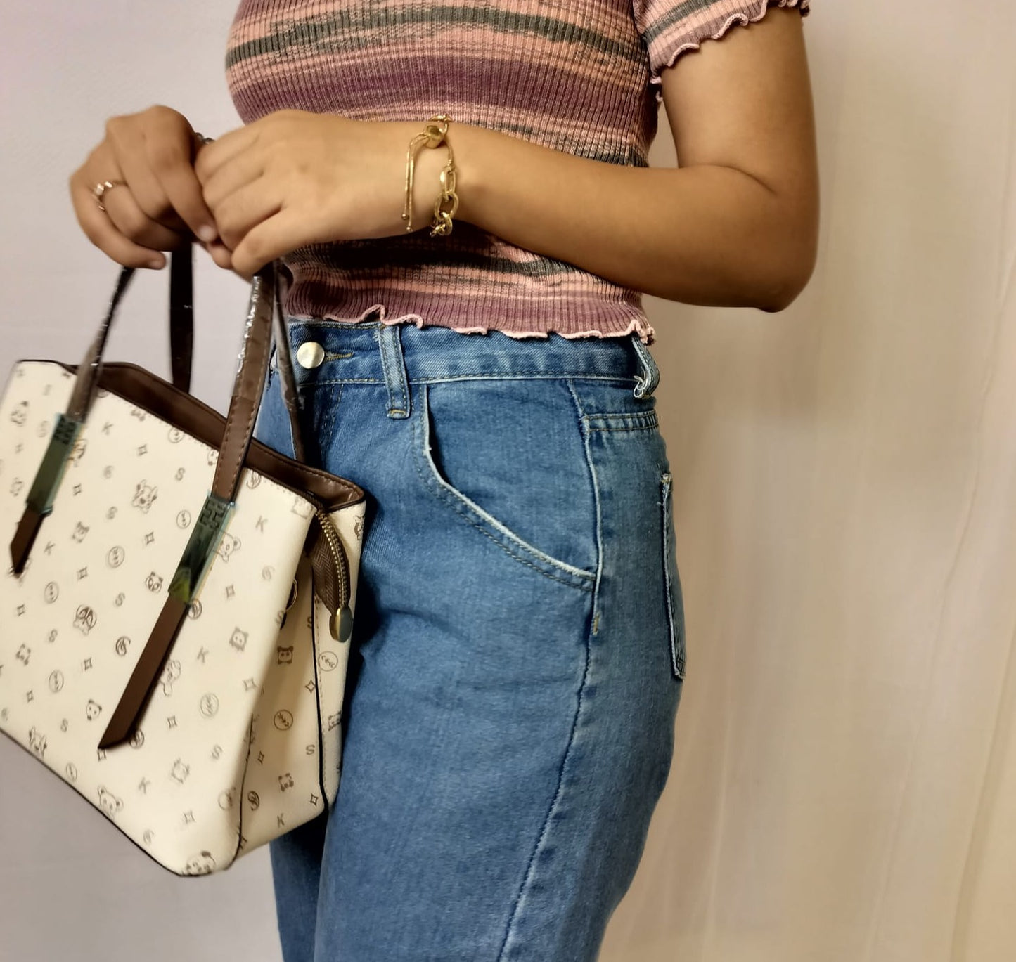 Woman holding a white and brown handbag wearing blue jeans and striped pink top green shoulder bag for women