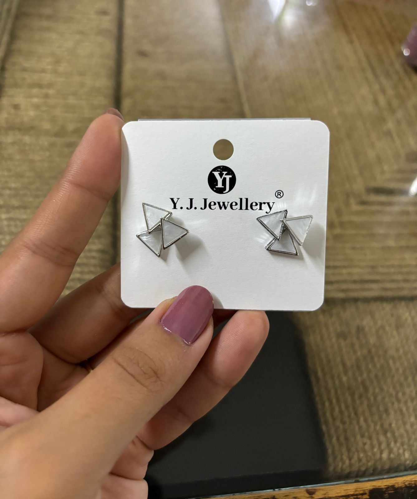 Korean triangle silver earrings displayed on white card held in hand by Wincham Fashion House