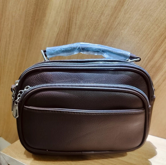 Brown leather bag with double zippered compartments and top handle wrapped in plastic