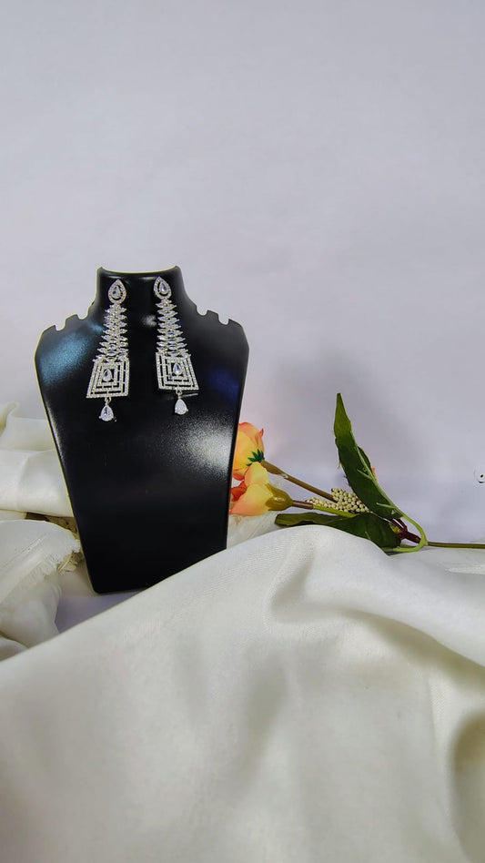 Designer American diamond dangle earrings displayed on a black stand with floral background