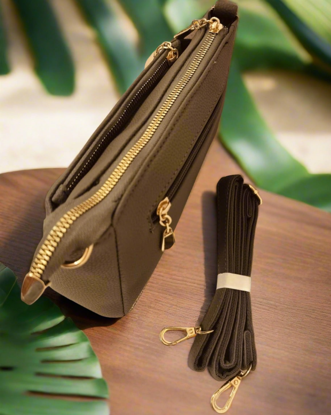 Women's crossbody bag grey with gold zippers and detachable strap on wooden surface