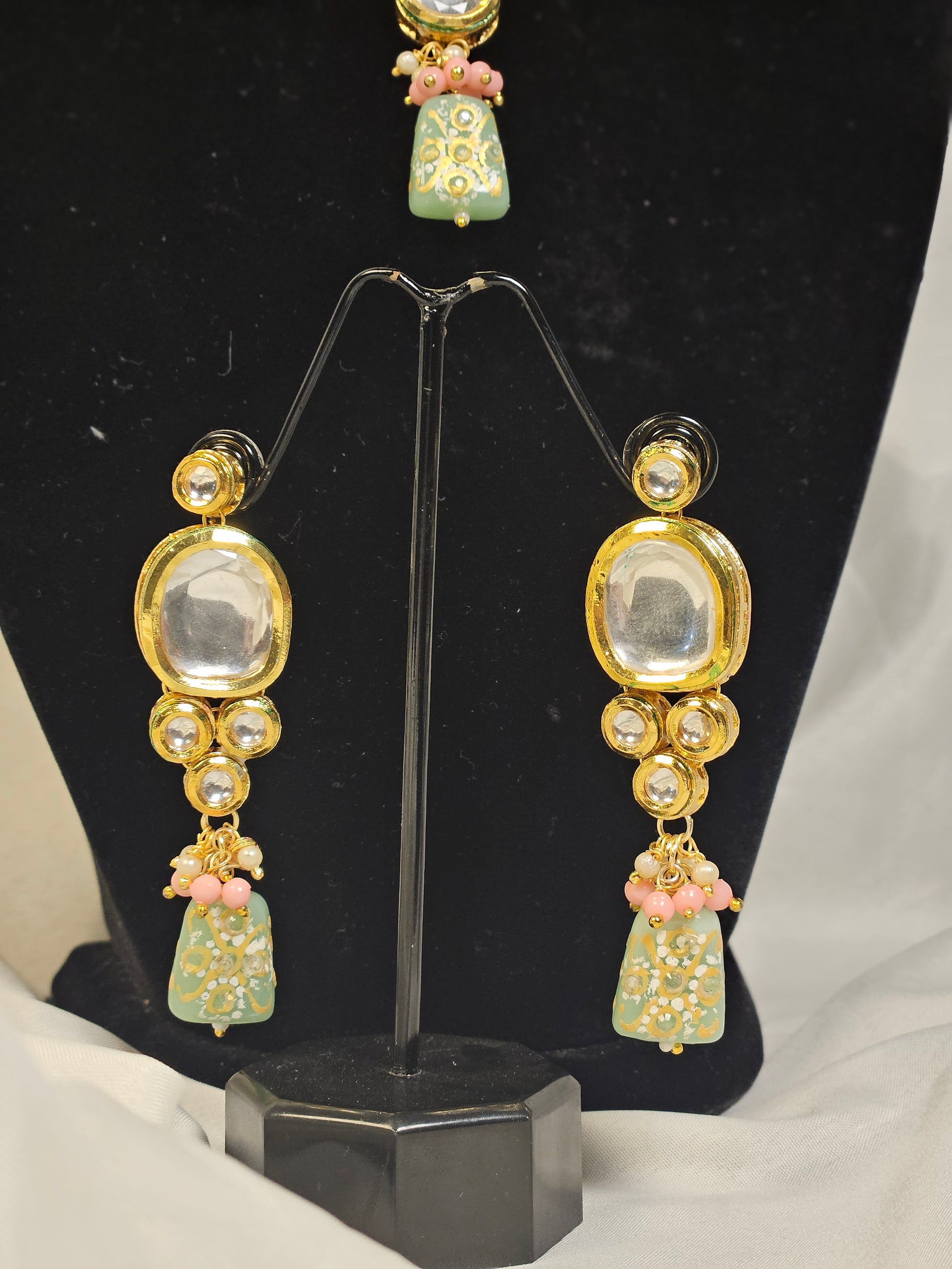 Pink and green Indian jewelry set featuring intricate earrings with gold and stone detailing