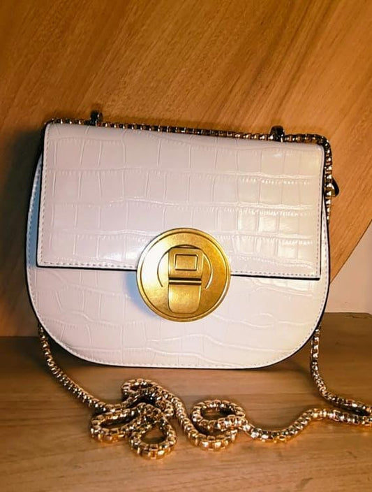 White party sling purse with gold circular clasp and chain strap on wooden surface